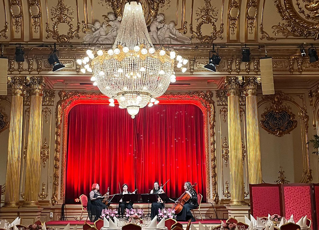 Orkester på scen med röd ridå bakom och stor kristallkrona framför